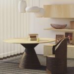 Modern dining room with a round wooden table, books on it, designer chairs, pendant lamps, and striped wall.