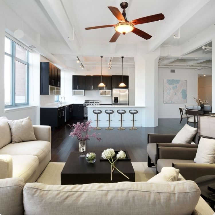 Modern open-plan living space with kitchen, island stools, sofa, and ceiling fan.